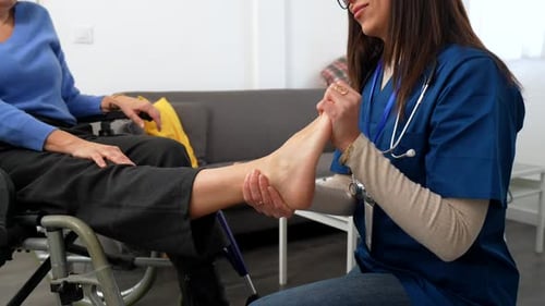 Caregiver Massaging the Foot of Woman in Wheelchair