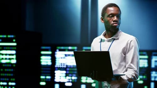 Focused Young Adult Male Holding Laptop in Server Room