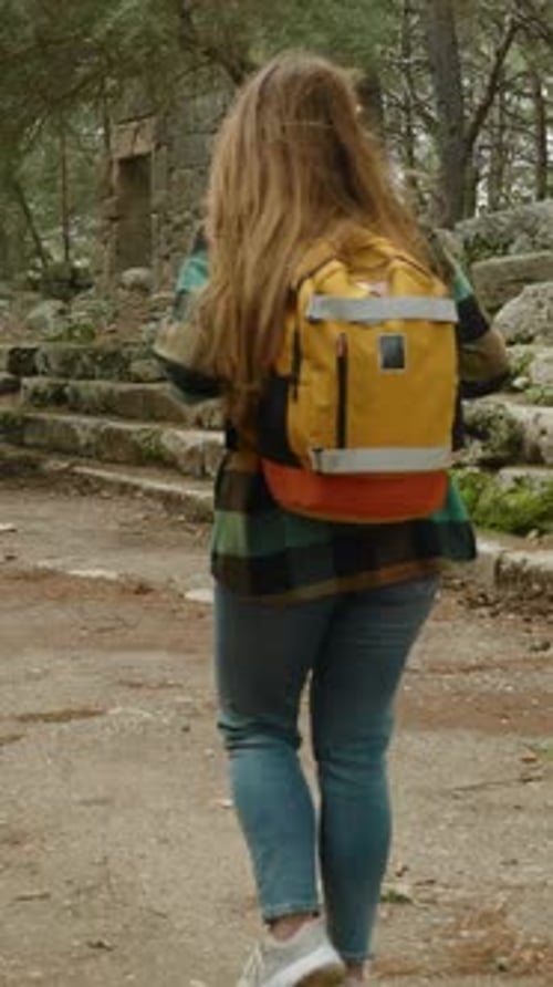 Vertical video. A female tourist with a backpack walks along the main street alongside the walls.