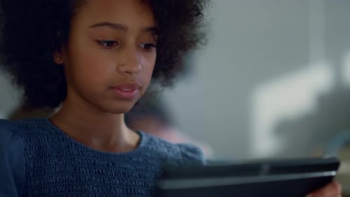 Serious Student Reading Book on Digital Tablet in School Classroom. African American