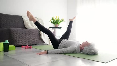 Senior Woman Exercising Legs on Yoga Mat Indoors