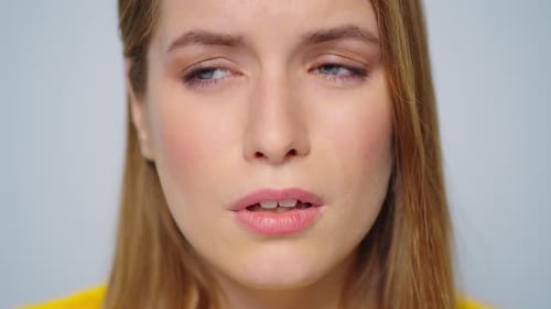 Nahaufnahme einer kranken Frau, die vor der Kamera niest, auf grauem Hintergrund. Nahaufnahme krank