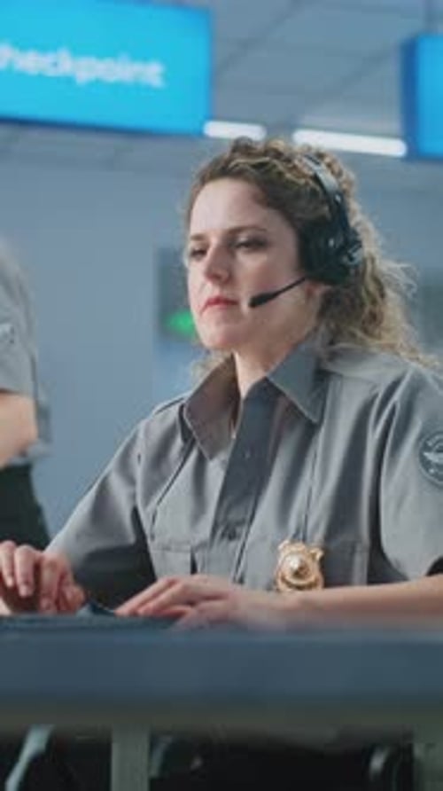 Airport Security Checkpoint Female Security Officer in Headset Using Laptop Looking at Camera