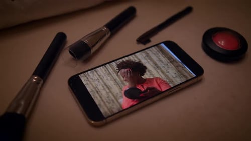 Smartphone Showing Woman Applying Makeup with Beauty Products