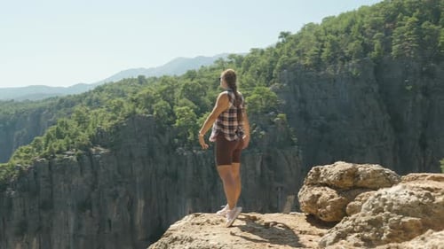 A Woman stands on a rocky cliff edge, her arms spread wide, facing the vast Canyon landscape. The ru