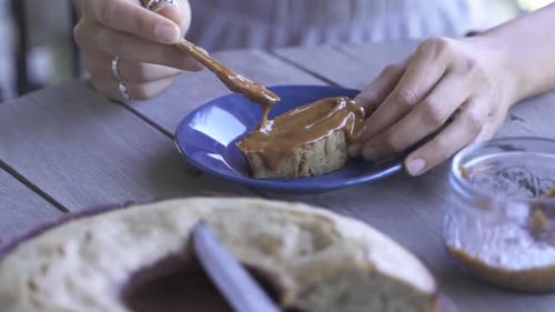 Nahaufnahme eines Weibchens, das Süßes auf Brot, Marmelade und Messer auf einem Holztisch im Freien verteilt Frühstück-Slow-Moti