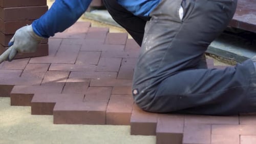 Closeup of a man setting brick pavers into place in a herringbone pattern.