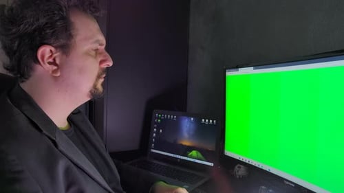 Closeup of a professional working on a computer with a green screen.