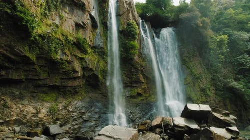 Close view of cascading waterfall over rocky cliffs by tropical forest