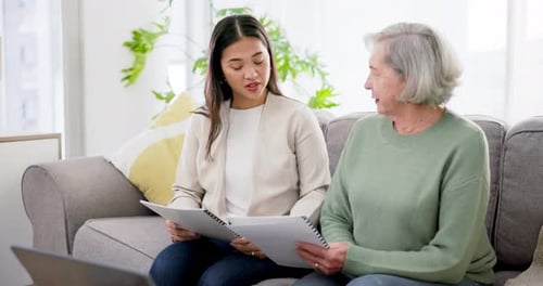 Two Women Discuss Documents on Couch at Home