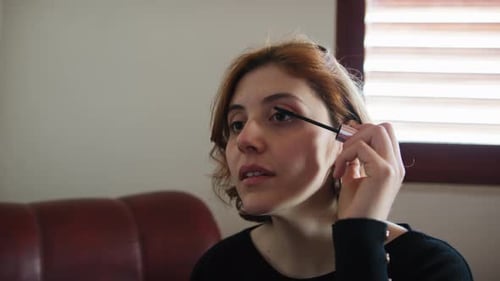 Woman Applies Mascara in Natural Light Indoors