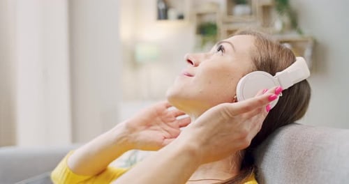 Linda jovem caucasiana sorriu mulher feliz em fones de ouvido descansando no sofá na aconchegante sala de estar e