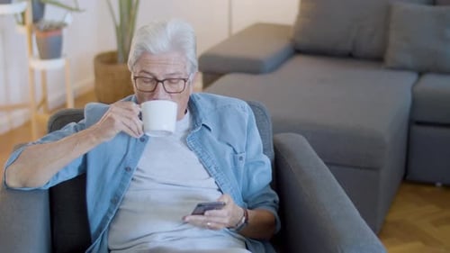 Senior Man Using Smartphone, Drinking Coffee Indoors