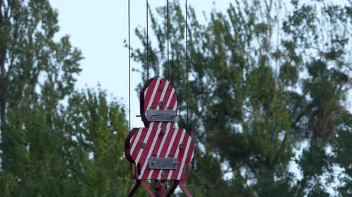 Pinzas de construcción rojas y blancas suspendidas por cables sobre un fondo de árboles, que indican constr