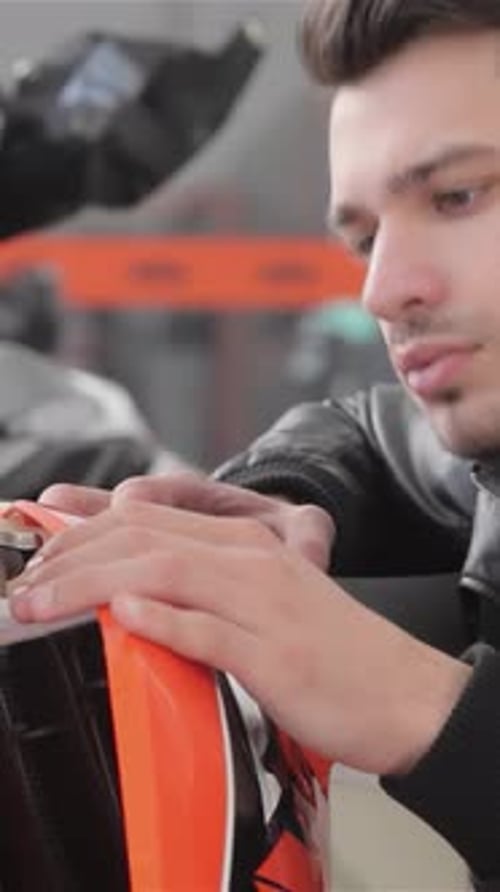 Young Man Inspects a Sleek Orange Sport Motorbike with Intense Fascination