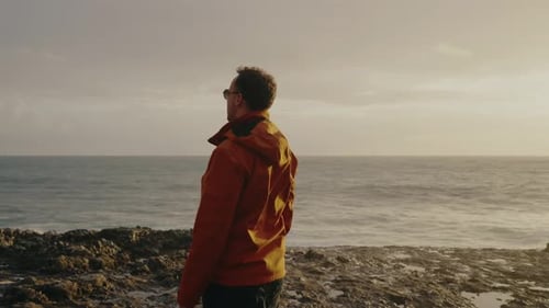 Man Contemplating the Ocean at Sunset in a Red Jacket