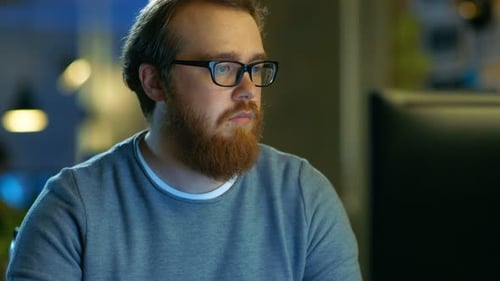 Der junge bärtige kreative Mann denkt über ein Problem nach, während er an seinem PC arbeitet.
