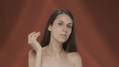 A Woman Takes Care of Her Skin Applies Cream on Her Face Portrait of a Young Seminude Woman in the