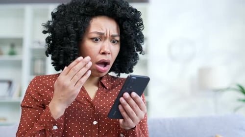 Close up. Disappointed young african american female reading bad news on smartphone while sitting