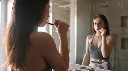 Young Woman Brushing Teeth in Bathroom Mirror
