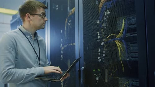 Dans un centre de données, un ingénieur informatique se tient devant un rack de serveurs en état de marche, effectue une vérification de maintenance de routine, un diagnostic