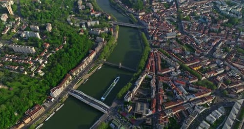 Drone de cima para baixo fotografado sobre a cidade ao pôr do sol ao longo de um rio azul Um navio turístico se move ao longo do rio Lyon