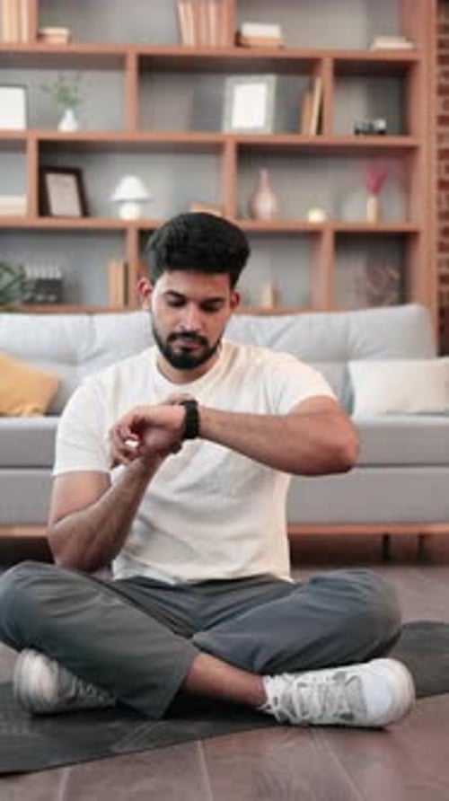 Man Sitting on Yoga Mat Using Smartwatch in Living Room