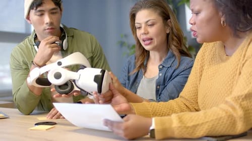 Des collègues diversifiés se réunissent à une table de bureau, examinent une feuille, passent un casque, évaluent la conception de la réalité virtuelle