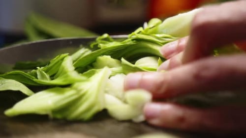 Asian chef finely chopping leafy green vegetables with a sharp knife.