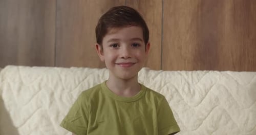 Retrato de un niño divertido, un niño sonriente mirando a la cámara está sentado en el sofá de su casa, un niño lindo