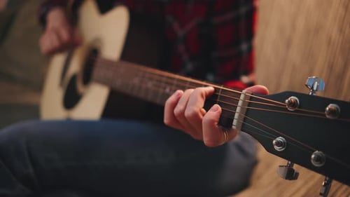 Close Up Strumming Acoustic Guitar on a Cozy Couch with Plaid Shirt and Denim Jeans in a Relaxed