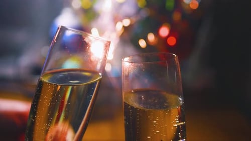 Taças de champanhe tilintando perto de uma árvore de Natal decorada e estrelinhas