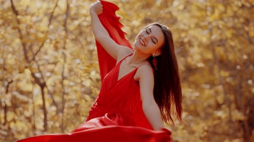 Beautiful Woman in a Red Dress Poses in a Bright Autumn Forest