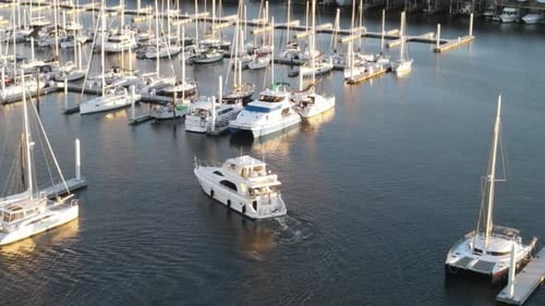 Luxury Motor Yacht Entering Marina With Moored Vessels During Sundown. - aerial