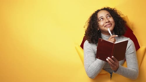 Creative Woman Writing in Notebook Through Yellow Background