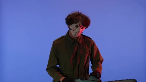 Man in White Mask with Chainsaw in Hands on Blue Background with Red Neon Light Image of Jason