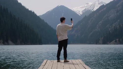 A Man on a Pier on a Mountain Lake A Guy Travels Alone Male Uses a Smartphone Takes Selfies