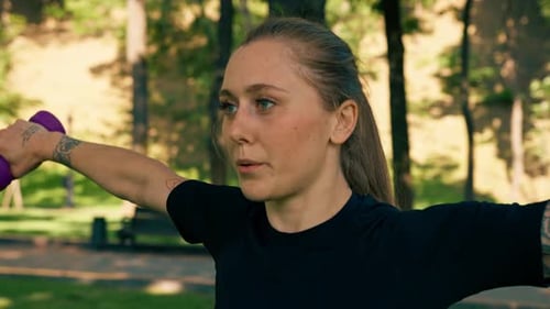 Woman Doing Arm Exercises with Dumbbells in Park
