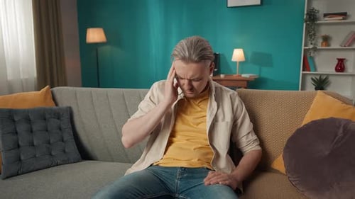 Medium Video of a Middleaged Man Sitting on a Couch Sofa Massaging His Temples and Head Due to a