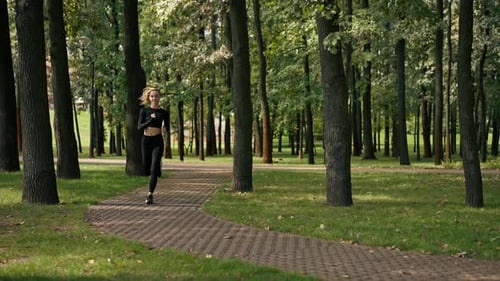 A young girl in sportswear and headphones runs in park in the morning to maintain physical fitness
