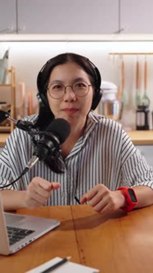Smiling woman recording podcast at table with laptop