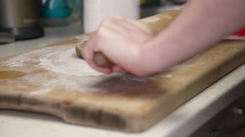 Caucasian woman dusting wooden board and working on gingerbread dough with a rolling pin.