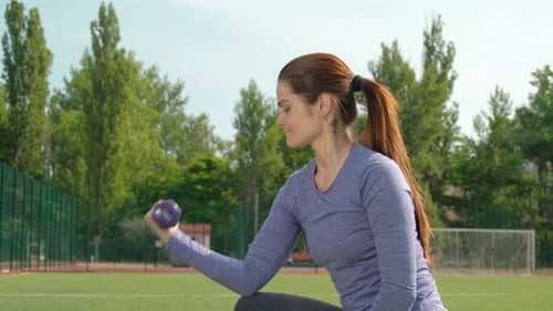 Fit Woman Does Bicep Curls with Dumbbell Outdoors