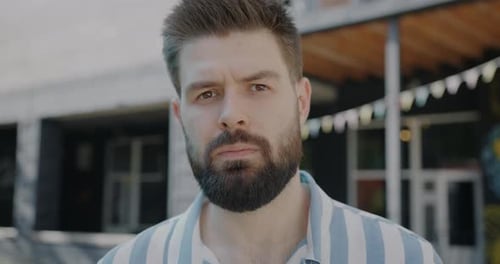 Retrato a cámara lenta de un joven serio mirando a la cámara al aire libre en un cálido día de verano