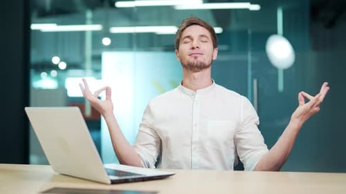 Young calm mindful man meditating doing yoga exercise sitting on the office, relax at work, peace