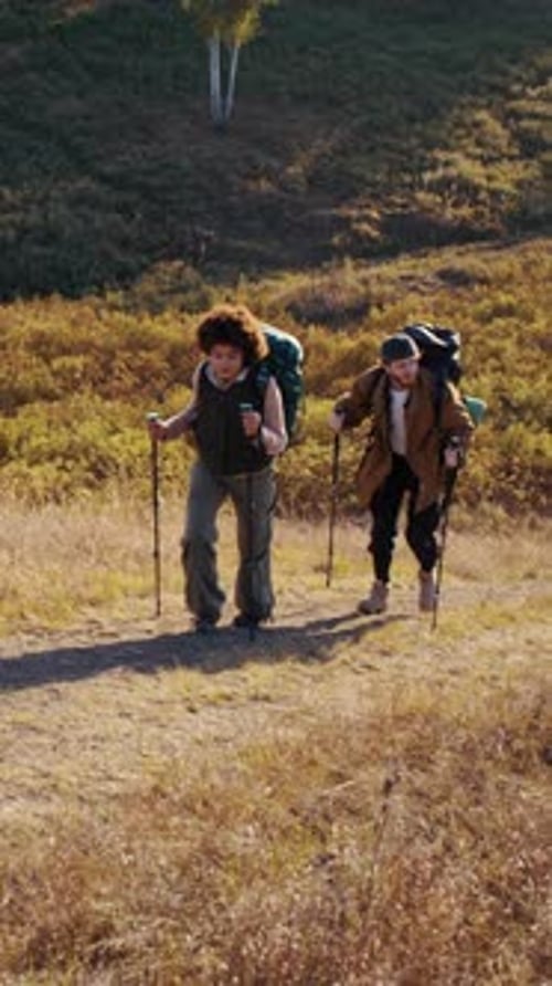 Pareja de excursionistas sube cuesta arriba apoyándose en bastones de marcha nórdica