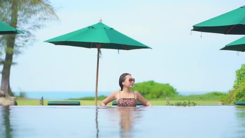 Asian model standing in swimming pool with sunglasses looking at tropical paradise landscape of isla