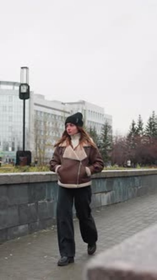 Young Girl Walking Slowly on Urban Autumn Pathway with Trees and City Buildings