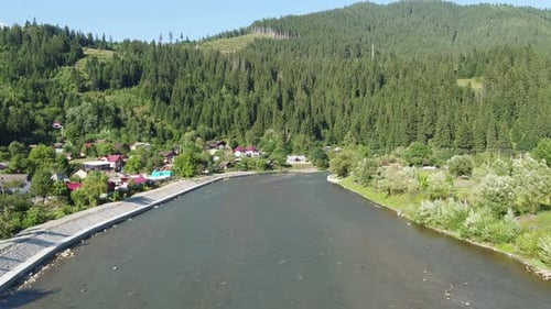 Mountain River Flows Past a Village Nestled in Dense Green Forest