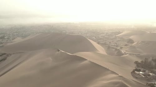 Aerial of people on sand dunes above Huacachina oasis, outside of Ica, Peru.